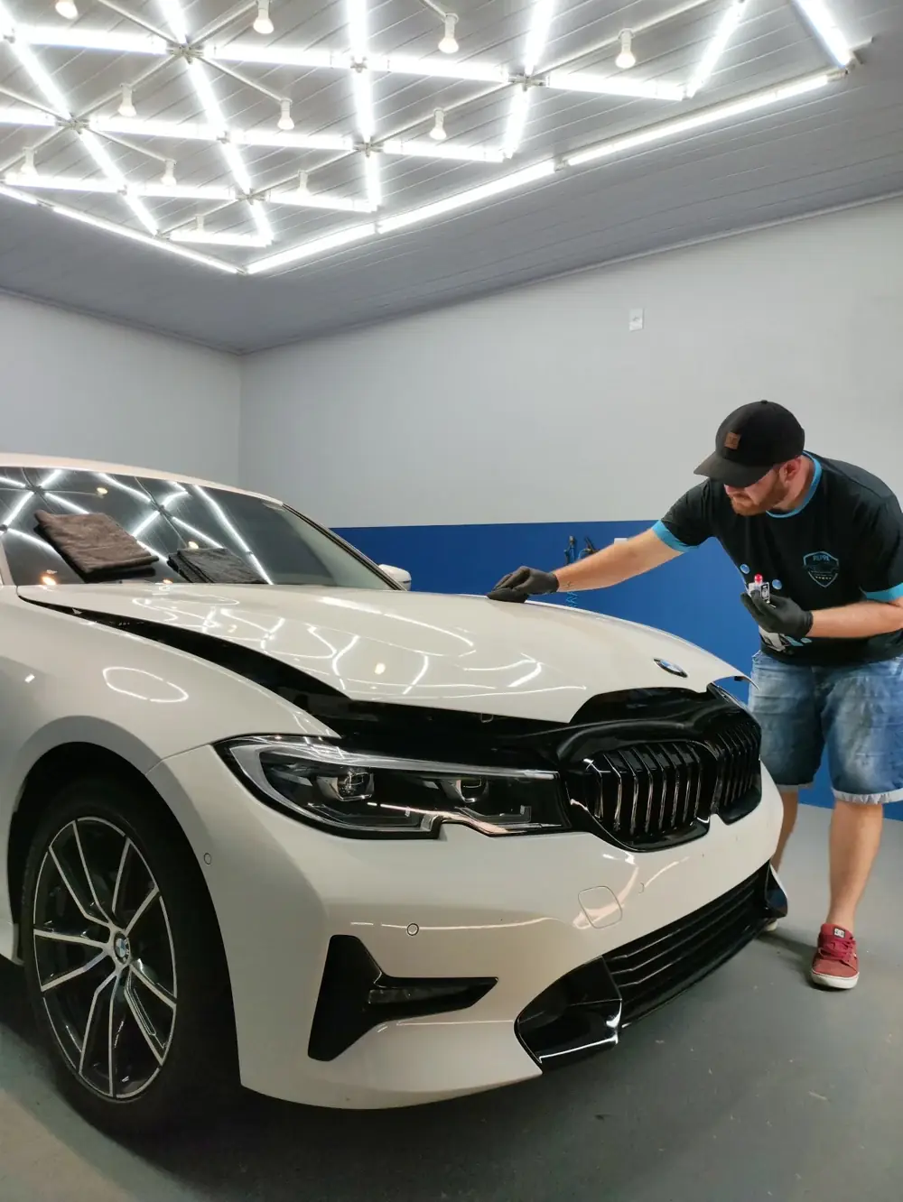 Profissional da Peppa cuidando manualmente do capô de um BMW branco