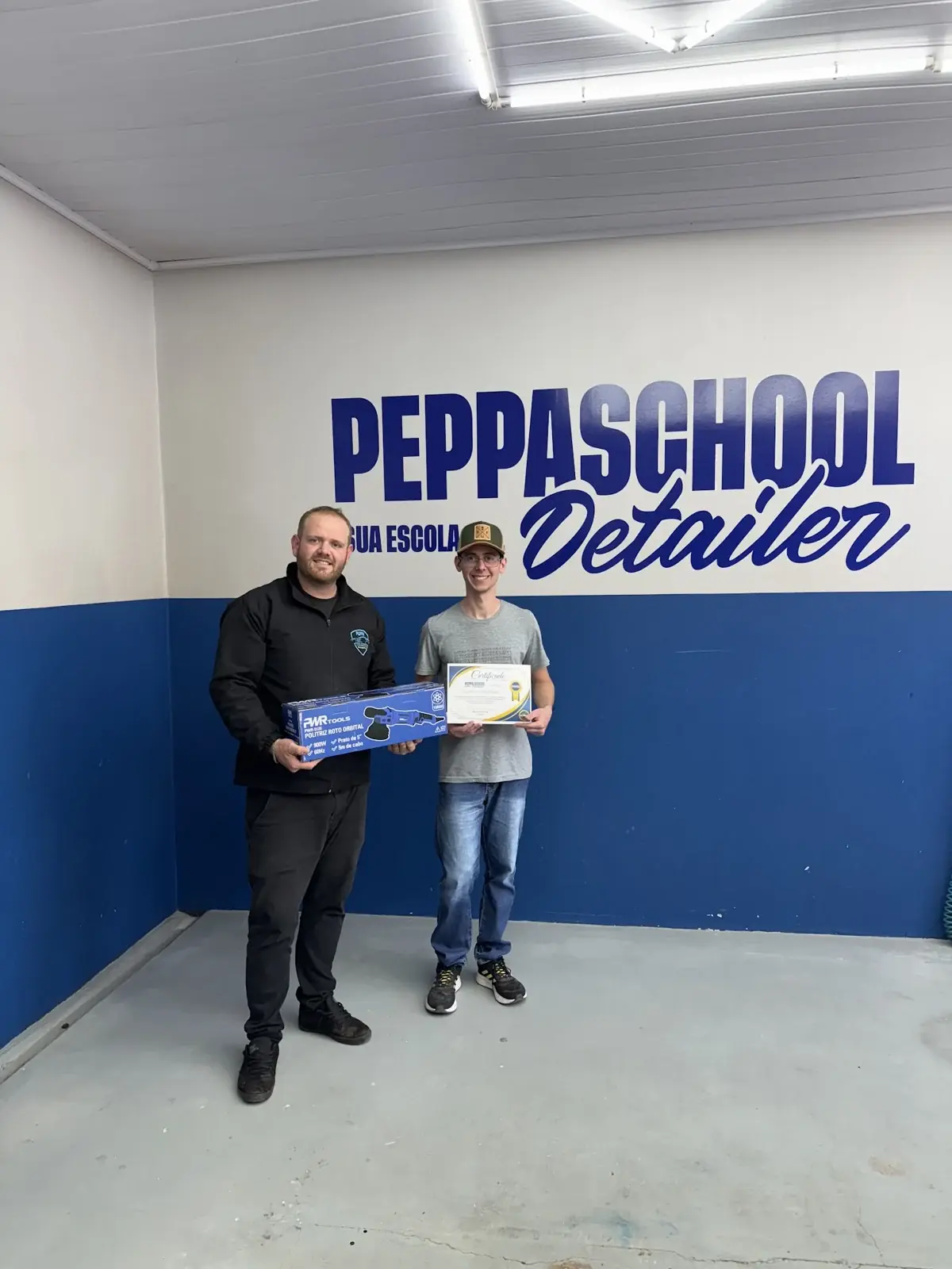 Profissional e aluno da Peppa School com certificado em frente à marca da escola